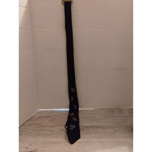 May include: A navy blue tie with a repeating pattern of small, colorful floral designs. The tie is hanging vertically against a white background. The tie has a gold-colored clasp at the top.