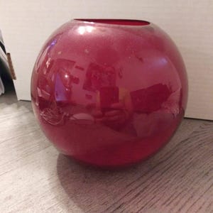 May include: A round, deep red glass vase with a smooth, shiny surface.