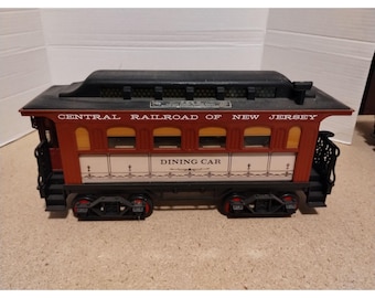 May include: A red and white model train carriage with black wheels. The carriage is labelled "Central Railroad of New Jersey" and "Dining Car".