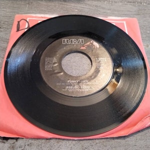 May include: Black vinyl record with a white label. The label has the text "RCA" in a red font, and the song title "FUNKYTOWN" from the album "Love An Adventure" by PSEUDO ECHO. The record is a 7-inch single and has the song title, artist, and record label information printed on the label.