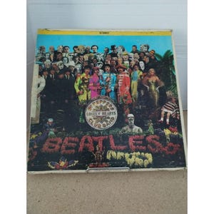 May include: A vintage vinyl record album cover featuring a colorful illustration of the Beatles band members surrounded by a variety of people and objects. The album title "Sgt. Pepper's Lonely Hearts Club Band" is prominently displayed in a circular design.