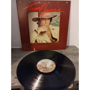 May include: A vinyl record album cover featuring a portrait of Tom Jones, a Welsh singer, wearing a brown cowboy hat and a fringed jacket. The album title "Darlin'" is printed in white letters on a red background.