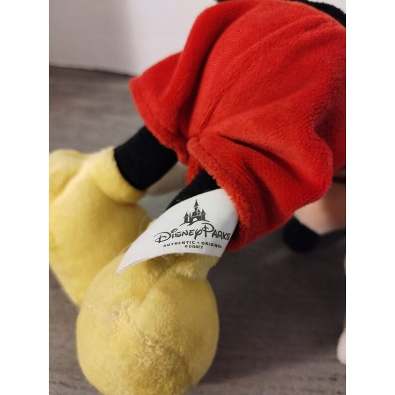 May include: A red and black plush Mickey Mouse toy with a yellow tag that reads "Disney Parks Authentic - Original &copy; Disney".