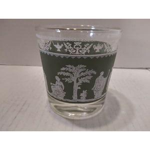 May include: A green glass tumbler with a white design of a tree and figures. The design is reminiscent of a Greek or Roman scene.