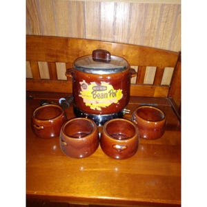 May include: A vintage brown and yellow electric bean pot with a metal lid and four matching brown ceramic bowls. The bean pot has a label that reads "West Bend Bean Pot".