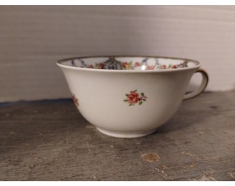 May include: A white porcelain teacup with a gold rim and floral pattern. The cup has a small handle and is decorated with pink and red roses.