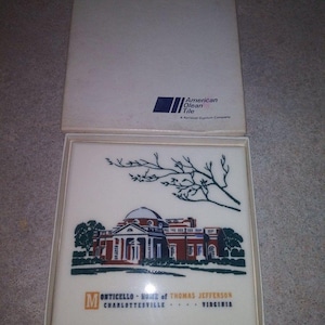 May include: A white tile featuring a detailed illustration of Monticello, the home of Thomas Jefferson, in Charlottesville, Virginia. The tile is in a box with the American Olean Tile logo and text. The image includes a tree branch design.