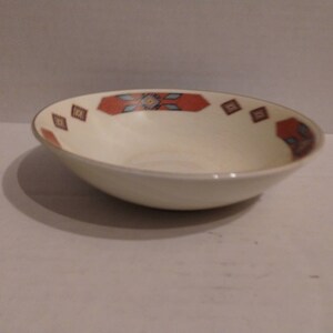 May include: A white ceramic bowl with a red, blue, and yellow geometric pattern around the rim.