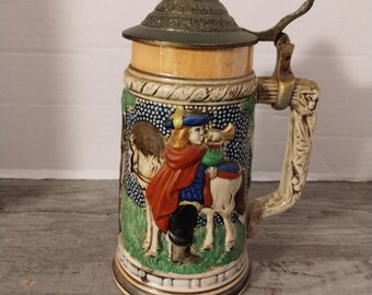 May include: A ceramic beer stein with a metal lid and handle. The stein features a colorful scene of a man on horseback playing a trumpet.