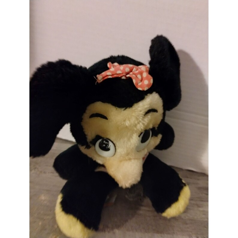 Puede incluir: Juguete de peluche negro y blanco con un lazo rosa con lunares blancos. El juguete tiene ojos grandes y una nariz peque&ntilde;a.