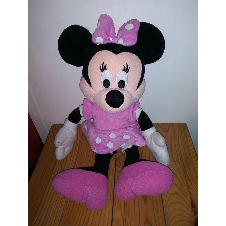 May include: A pink and white polka dot dress with a pink bow on top of the head. The plush toy is a cartoon character with black ears and a black nose.