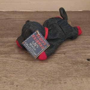 May include: A denim plush toy in the shape of an animal, possibly a dog or a pig, with red accents on the feet and around the body. The toy has a tag that reads "Floppy Friends Denim Collection!"