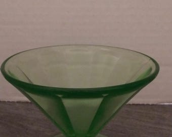 May include: A green glass dessert dish with a fluted design. The dish has a wide, shallow bowl and a short stem.