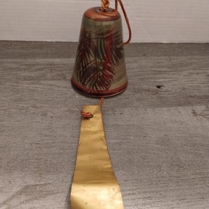 May include: A ceramic wind chime with a brown, green, and red leaf pattern. The chime has a gold metal clapper and a brown cord.