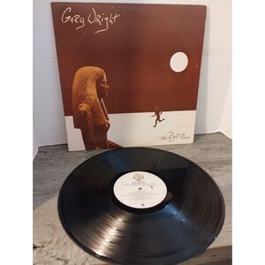 May include: A vinyl record album cover featuring a brown background with a white moon and a running figure. The album title is "The Right Place" and the artist is "Gary Wright".