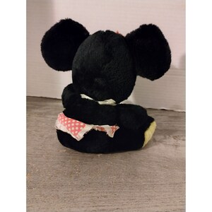 Puede incluir: Juguete de rat&oacute;n de peluche negro con falda de tela de lunares rojos. El rat&oacute;n est&aacute; sentado de espaldas a la c&aacute;mara.
