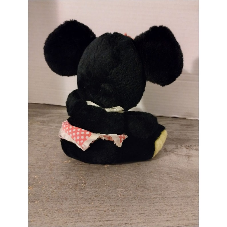Puede incluir: Juguete de rat&oacute;n de peluche negro con falda de tela de lunares rojos. El rat&oacute;n est&aacute; sentado de espaldas a la c&aacute;mara.