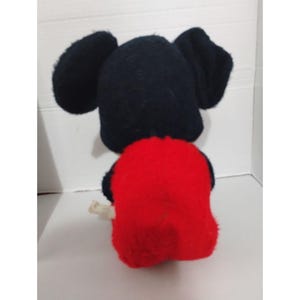 May include: A plush toy of Mickey Mouse sitting down. The toy is black and red with large black ears.