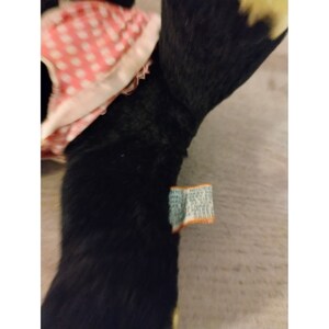 Puede incluir: Juguete de peluche negro y blanco con un vestido a cuadros rosa y blanco. El juguete tiene una etiqueta amarilla unida a su brazo que dice "Melissa & Doug".