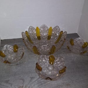 May include: A set of four glass bowls with a clear body and yellow accents. The bowls are decorated with a delicate pattern and have a scalloped edge.