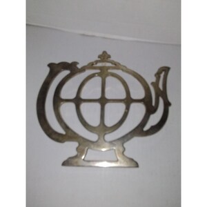May include: Silver teapot-shaped hot pad with a circular design in the center.