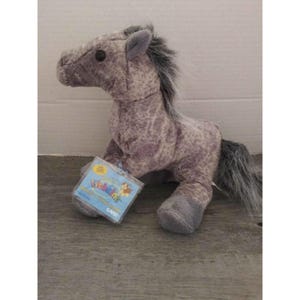 May include: A plush horse toy in shades of gray and purple, with a dark gray mane and tail. The toy has a tag attached with the words "Webkinz" and "Game" visible. The horse is in a seated position.