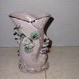 May include: A pink ceramic vase shaped like a fish with a raised, textured surface. The vase has a green and white floral design on the side.