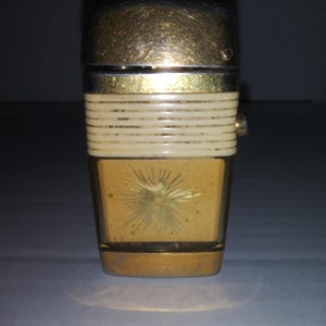 May include: A gold and white vintage lighter with a starburst design. The lighter has a textured white band around the middle.