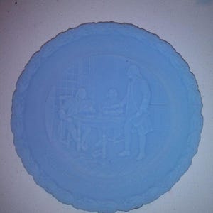 May include: A light blue decorative plate with a detailed relief scene of figures around a table, likely depicting a historical event. The plate has a scalloped edge and the year "1776" is visible. The plate is round.