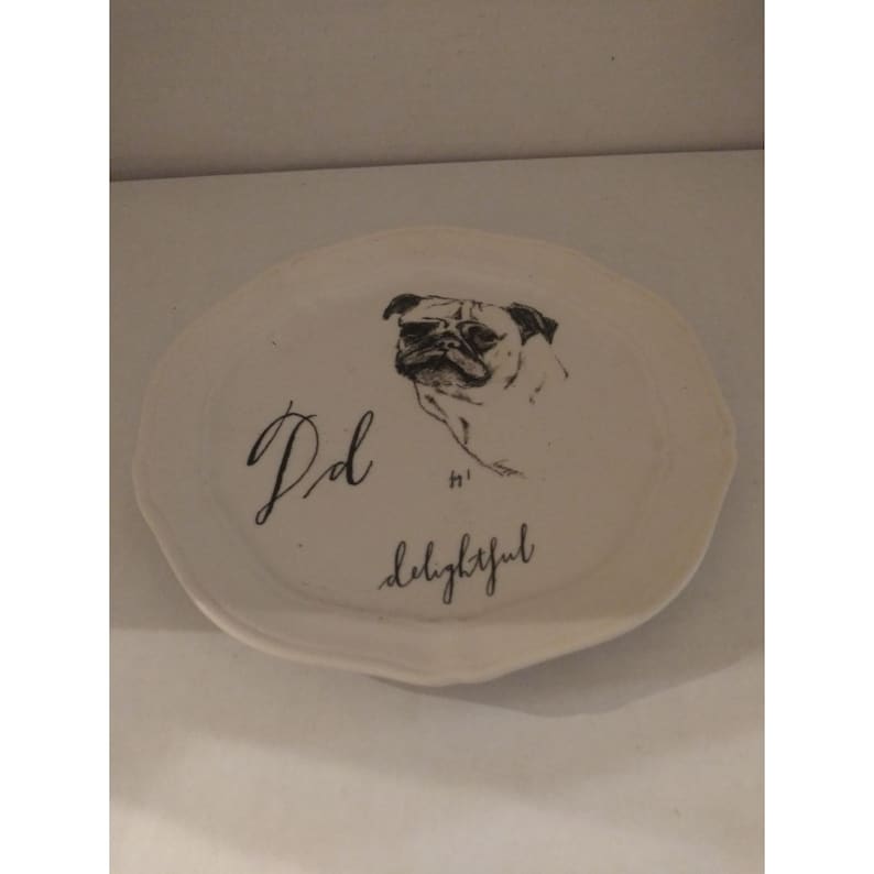 K&ouml;nnte beinhalten: Wei&szlig;e Keramikplatte mit einer Schwarzwei&szlig;illustration eines Mops. Die Platte tr&auml;gt den Text "Pd" und "so delightful".
