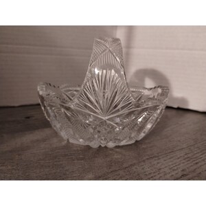 May include: A clear glass bowl with a cut glass design and a handle. The bowl is perfect for serving fruit or snacks.