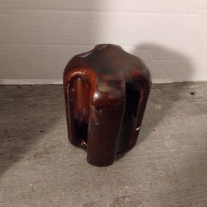 May include: A brown ceramic insulator with four holes for wires. The insulator has a rough, textured surface.