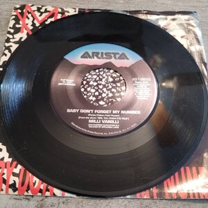 May include: Black vinyl record with a white label. The label has a pink and blue mountain scene with a black and white pattern. The text on the label reads "Arista", "AS1-9832", "Time: 40", "Produced and", "Baby Don't Forget My Number", "Ferien/Deltion/Nail/Reuter", "From the album "Girl You Know It's True", "Milli Vanilli", "Unauthorized Duplication is a Violation of Applicable Laws", "Manufactured by Arista Records, Inc. 6 W 57th St. NY, NY 10019".