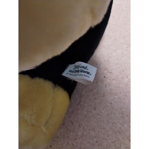 May include: A black and yellow plush toy with a white tag that reads "Disneyland Walt Disney World" and "Walt Disney Productions".