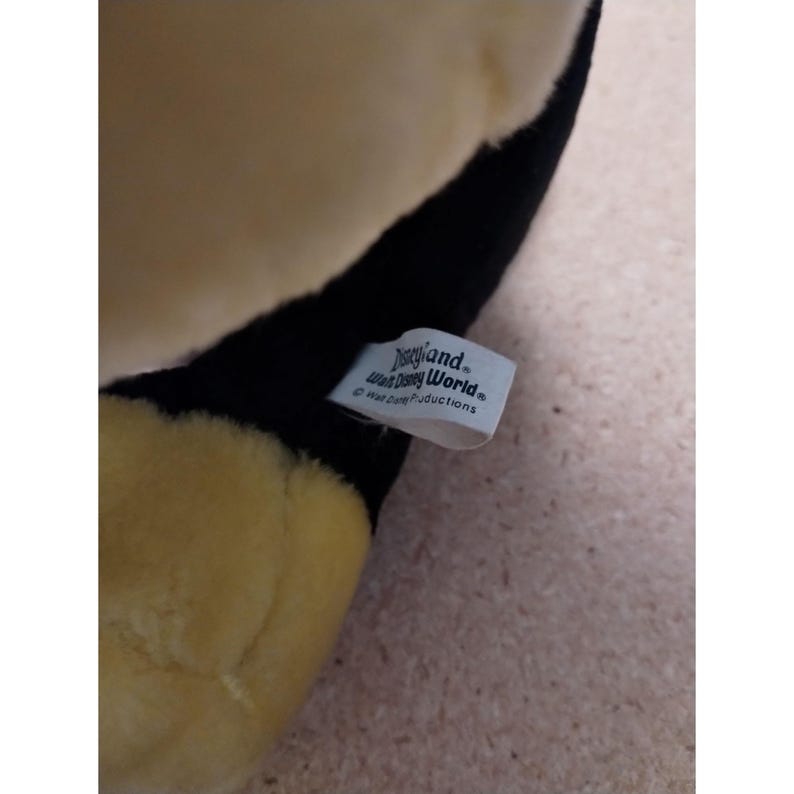 May include: A black and yellow plush toy with a white tag that reads "Disneyland Walt Disney World" and "Walt Disney Productions".