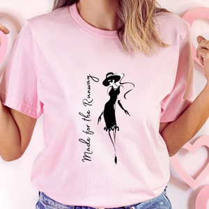 May include: Pink t-shirt with a black graphic of a woman in a dress and hat. The text "Made for the Runway" is printed vertically on the left side of the shirt.