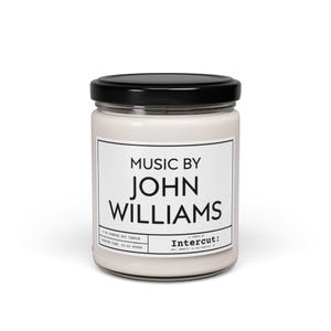 Może przedstawiać: Biała świeca w szklanym słoiku z czarną pokrywką. Etykieta zawiera napis "Music by John Williams" i "A candle by Intercut: Est. 2020 in Los Angeles, CA".