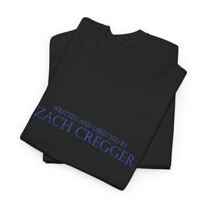 Pode incluir: Uma t-shirt preta com o texto azul WRITTEN AND DIRECTED BY ZACH CREGGER impresso na frente. A peça está dobrada, exibindo uma gola redonda e mangas curtas, com o texto claramente visível numa fonte sem serifa.