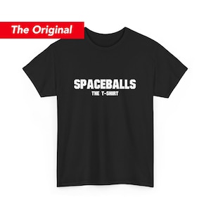 May include: Black t-shirt with the text "SPACEBALLS THE T-SHIRT" in white block letters. The words are centered on the front of the shirt. A red rectangle with the words "The Original" is in the upper left corner.