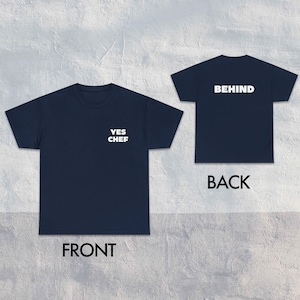 May include: A navy blue t-shirt with the text "YES CHEF" printed on the front and "BEHIND" printed on the back.
