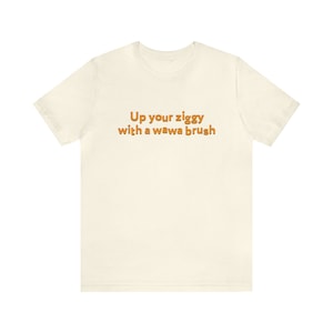 May include: A white t-shirt with the text "Up your ziggy with a wawa brush" printed in orange.