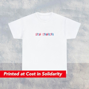 Puede incluir: Camiseta blanca con el texto "PAY ACTORS" impreso en letras rojas y azules.