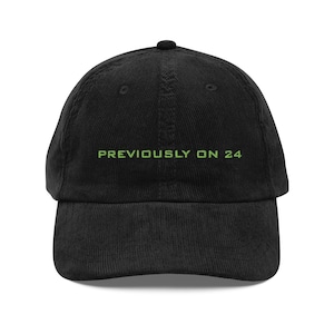 May include: Black corduroy baseball cap with the text "PREVIOUSLY ON 24" in green lettering across the front. The cap has a curved brim and a button on top.