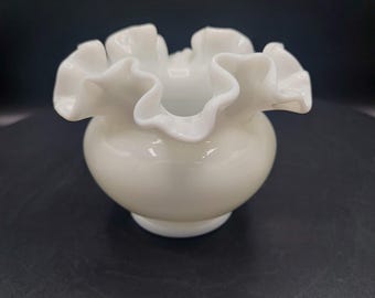 May include: A white ruffled glass vase with a round body. The vase is made of opaque glass and has a smooth, glossy finish.