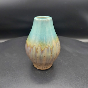 May include: A small, teal-colored ceramic vase with a brown and white glaze. The vase has a rounded body and a narrow neck.