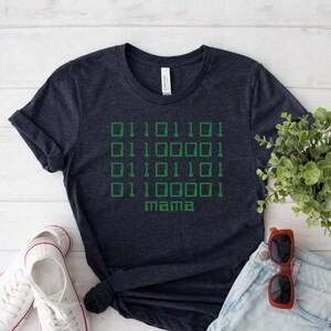 May include: A dark blue t-shirt with a green binary code design and the word "mama" printed on the front.