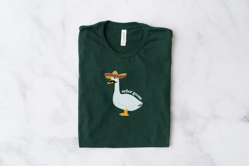 May include: A dark green t-shirt featuring a white goose wearing a sombrero and a moustache. The text "senor goose" is printed below the goose.