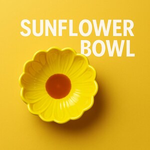 May include: A yellow ceramic bowl shaped like a sunflower with a brown center. The bowl is on a yellow background with the text "SUNFLOWER BOWL" in white.
