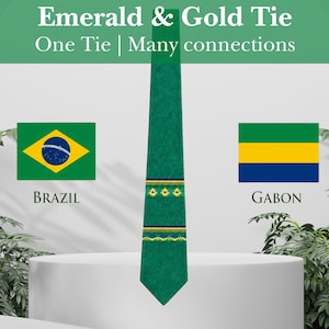 May include: An emerald green necktie featuring a horizontal band with small yellow flower motifs and dark blue accents. The text "Emerald & Gold Tie" and "One Tie | Many connections" appears above, with the flags of Brazil and Gabon displayed.