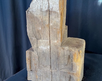 Può includere: Un blocco di legno grezzo e invecchiato con una finitura naturale e rustica. Il blocco ha una forma unica e irregolare con una parte superiore piatta e larga e una base rettangolare più piccola. Il legno è di colore marrone chiaro con aree di marrone scuro e grigio.